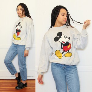 May include: A gray sweatshirt with a vintage Mickey Mouse graphic. The sweatshirt has long sleeves and a crew neck. The Mickey Mouse graphic is in red, black, and yellow.