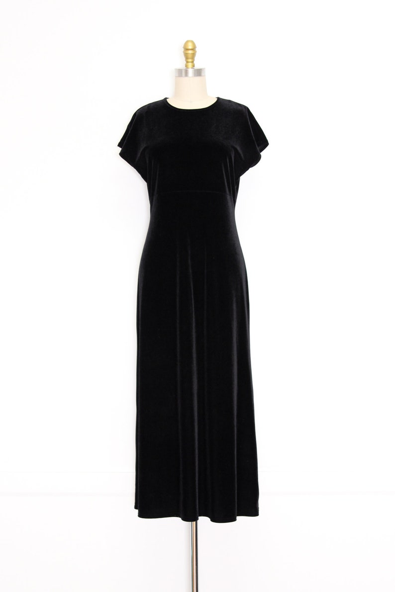 Puede incluir: Un vestido maxi de terciopelo negro con mangas cortas y cuello redondo. El vestido est&aacute; en un maniqu&iacute;.