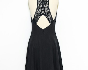May include: A black sleeveless dress with a lace back detail. The lace is a delicate pattern of swirls and circles.