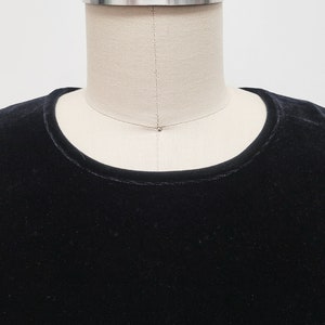 Puede incluir: Una camisa de terciopelo negro con cuello redondo.
