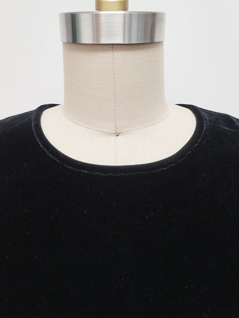 Puede incluir: Una camisa de terciopelo negro con cuello redondo.