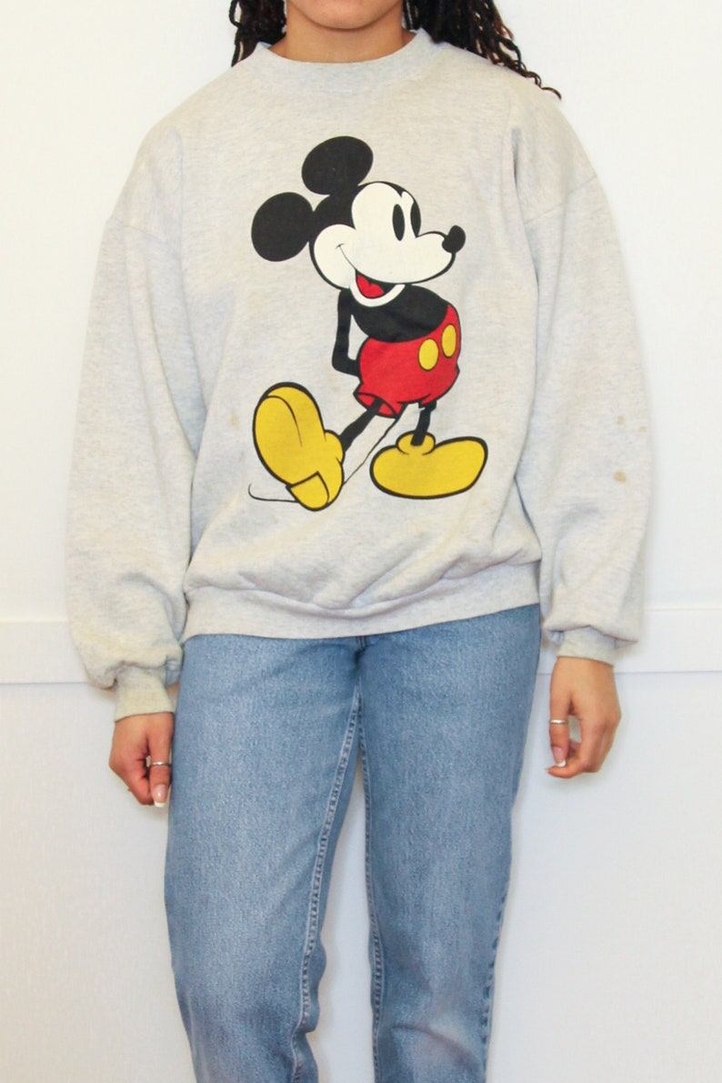 May include: A gray sweatshirt with a cartoon image of Mickey Mouse in a red and yellow outfit.