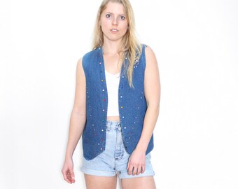 May include: A blue denim vest with colorful embellishments. The vest has a V-neck and a button closure.