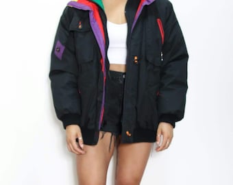 May include: Black puffer jacket with a colourful striped inner lining. The lining features yellow, green, purple and red stripes. The jacket has a zip closure and multiple pockets.