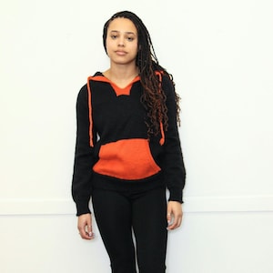 May include: A black and orange hooded sweater with a large pocket on the front. The sweater is made of a soft, fuzzy material.