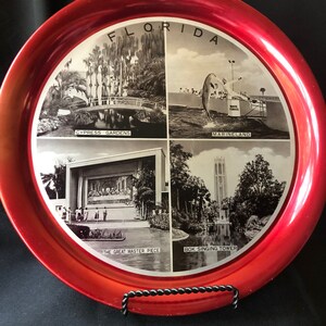 May include: Red metal tray with four black and white images of Florida attractions. The images are labeled "Cypress Gardens", "Marineland", "The Great Master Piece", and "Bok Singing Tower". The tray has a red rim and the word "FLORIDA" in white letters.