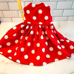 May include: A red sleeveless dress with white polka dots. The dress has a gathered skirt and a simple neckline.