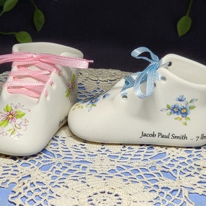 May include: Two porcelain baby shoes with blue and pink ribbons. The blue shoe has forget-me-not flowers and the text "Jacob Paul Smith -- 7 lbs. 1"