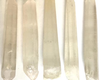 May include: Five clear quartz crystal points of varying shapes and sizes are arranged vertically. Each crystal has a natural, translucent appearance, with visible internal structures. The crystals are labeled A through E at the base.