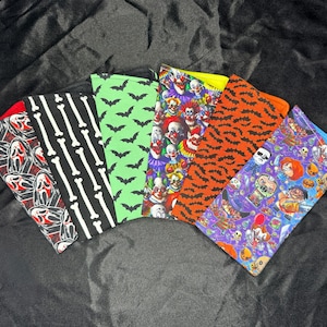 May include: A collection of Halloween-themed face coverings. Designs include a red and black Scream mask pattern, black and white bones, green bats, clown faces, orange tiger stripes, and a purple monster mash design.