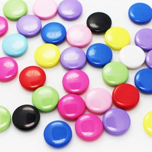 May include: A selection of brightly coloured, round buttons in shades of red, blue, green, yellow, pink, purple, black, and white. The buttons are scattered on a white surface, creating a vibrant display. These buttons are suitable for crafts and sewing projects.