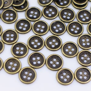 May include: A large group of antique gold metal buttons with four holes each. The buttons are scattered on a white surface.