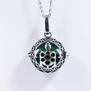 May include: Silver necklace with a round pendant featuring a green turtle design. The pendant is a cage-like design with a small bell inside.