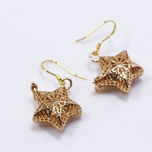 May include: A pair of gold star-shaped earrings with a delicate, intricate design. The earrings are made of a lightweight metal and have a simple hook fastening.
