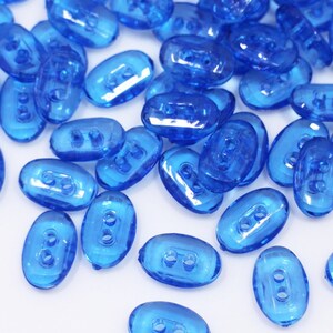 May include: A large group of blue plastic buttons with two holes each. The buttons are oval shaped and have a glossy finish.
