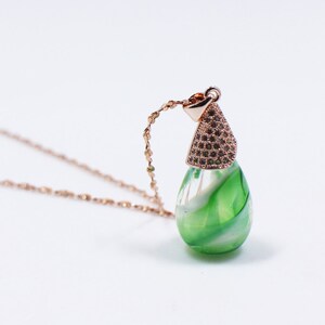 May include: A delicate gold chain necklace with a green and white swirl glass pendant. The pendant has a rose gold top with a diamond-like pattern.