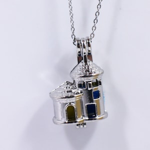 May include: Silver necklace with a charm shaped like a small castle with blue and yellow accents.