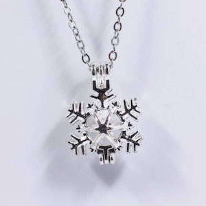 May include: A silver snowflake charm necklace with a delicate chain. The charm is open and can be used to hold a small object, such as a pearl or a crystal.