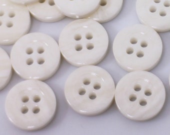 May include: A collection of white, round buttons with four holes each. The buttons are made of a smooth, slightly iridescent material.