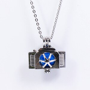 May include: A silver chain necklace with a silver charm pendant. The charm is shaped like a small cage with a blue star inside.