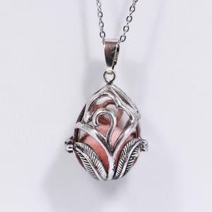 May include: A silver pendant necklace with a delicate, openwork design in the shape of a teardrop. The pendant has a small, pink stone inside.