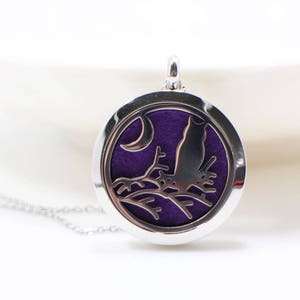 May include: A silver necklace with a round pendant featuring a purple silhouette of a cat perched on a branch under a crescent moon.