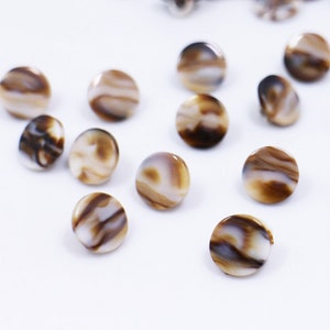 May include: A collection of brown and white shell buttons with a marbled pattern.
