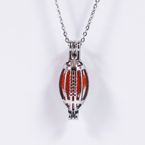 May include: A silver necklace with a football-shaped cage pendant. The cage is open and has a red interior.