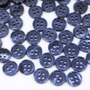 May include: A large group of blue plastic buttons with four holes each. The buttons are scattered on a white surface.