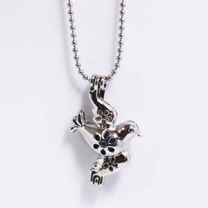 May include: A silver chain necklace with a silver dove pendant. The dove has a detailed design with blue flowers on its wings and body.