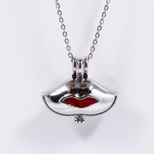 Könnte beinhalten: Eine silberne Halskette mit einem Anhänger in Form von Lippen. Die Lippen sind rot und der Anhänger ist offen, um ein kleines Fach zu enthüllen.