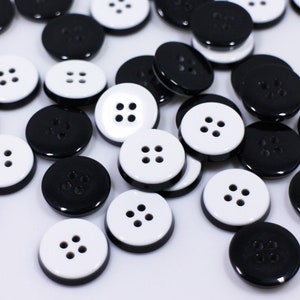 May include: A collection of black and white buttons with four holes each. The buttons are arranged in a random pattern on a white surface.