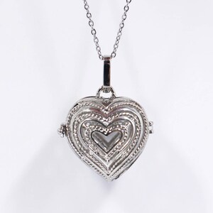 Peut inclure: Un collier avec un pendentif en forme de cœur argenté orné d'un motif détaillé. Le pendentif a une ouverture à charnière et une chaîne délicate.