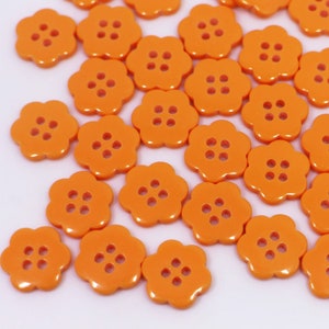 以下が含まれることがあります： 4つの穴のあるオレンジ色のプラスチック製のフラワー型のボタンの詰め合わせです。