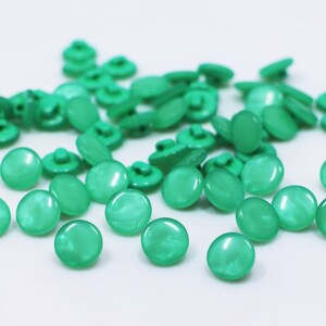 May include: A collection of green plastic buttons with a pearlescent finish. The buttons are round and have a flat back.