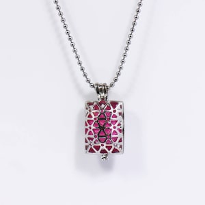 May include: A silver chain necklace with a pink and silver pendant. The pendant is a rectangular cage with a geometric design.