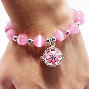 May include: A pink gemstone bracelet with a silver charm. The charm is a cage with a flower design.