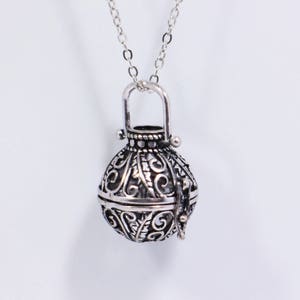 May include: A silver filigree pendant necklace with a round, openwork cage design. The cage is attached to a silver chain.