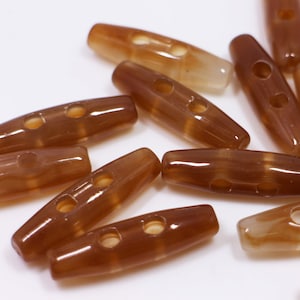 May include: A group of brown plastic toggle buttons with two holes each. The buttons are translucent and have a glossy finish.