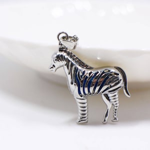 May include: A silver zebra pendant with a detailed design. The pendant is on a white surface.