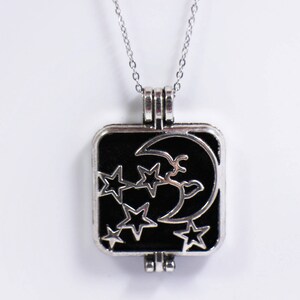 May include: A silver necklace with a black square pendant featuring a crescent moon and stars. The pendant is open on the side and has a hinge.