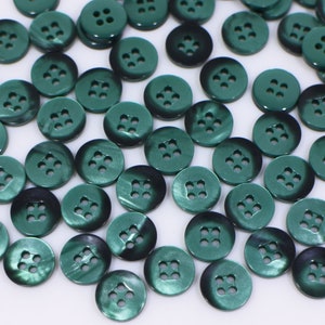 以下が含まれることがあります： 4つの穴のある緑色のプラスチックボタンがたくさんあります。ボタンは光沢のある金属仕上げです。