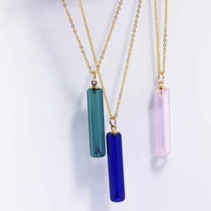 May include: Three gold chain necklaces with different coloured glass pendant charms. The charms are long and rectangular, with one blue, one teal, and one pink.