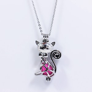 May include: A silver charm necklace featuring a cat-shaped pendant. The pendant is open and has a pink interior. The chain is silver and has a delicate design.
