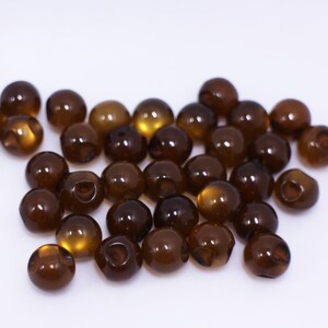 May include: A group of brown plastic beads, some with a slight amber hue, scattered on a white surface.