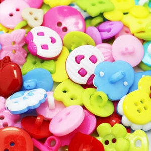 May include: A large assortment of colourful plastic buttons in various shapes and sizes. The buttons feature different designs, including stars, hearts, flowers, and smiley faces.