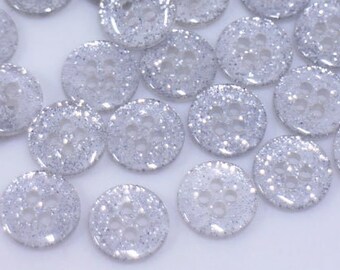 May include: A large group of silver glitter buttons. The buttons are round and have a clear plastic base with silver glitter embedded in the plastic.