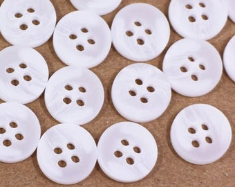 May include: A collection of white plastic buttons with four holes each. The buttons are arranged in a circular pattern on a brown surface.