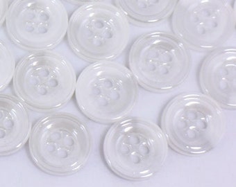 May include: A large group of white plastic buttons with four holes each. The buttons are arranged in a random pattern on a white surface.