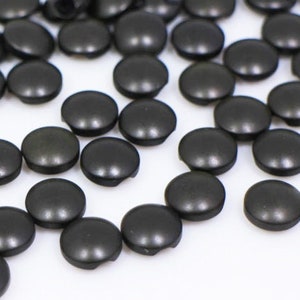 May include: A large quantity of black plastic buttons. The buttons are round and have a flat top.